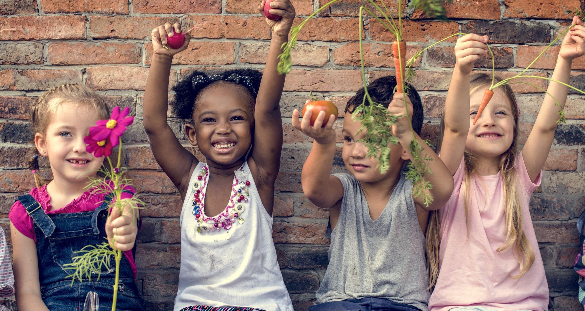 Four young children holding items that have been grown in a garden.