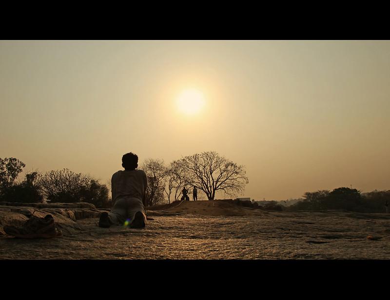 Man laying on the ground looking out into the landscape of trees with the sun shining. 