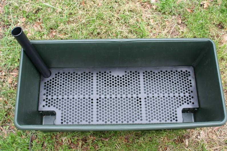 Top view of an empty EarthBox planter, showing a perforated plastic plate that separates the potting mix area from the water reservoir in the base.