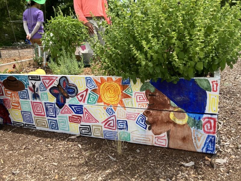 Side view of a raised bed painted with multiple colorful geometric designs, a sun, a person’s profile, and a butterfly.