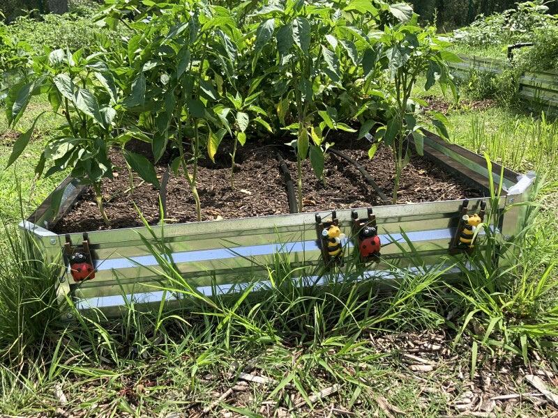 Corrugated metal panels form the walls of a raised bed, custom-decorated with ladybug and bee figurines.