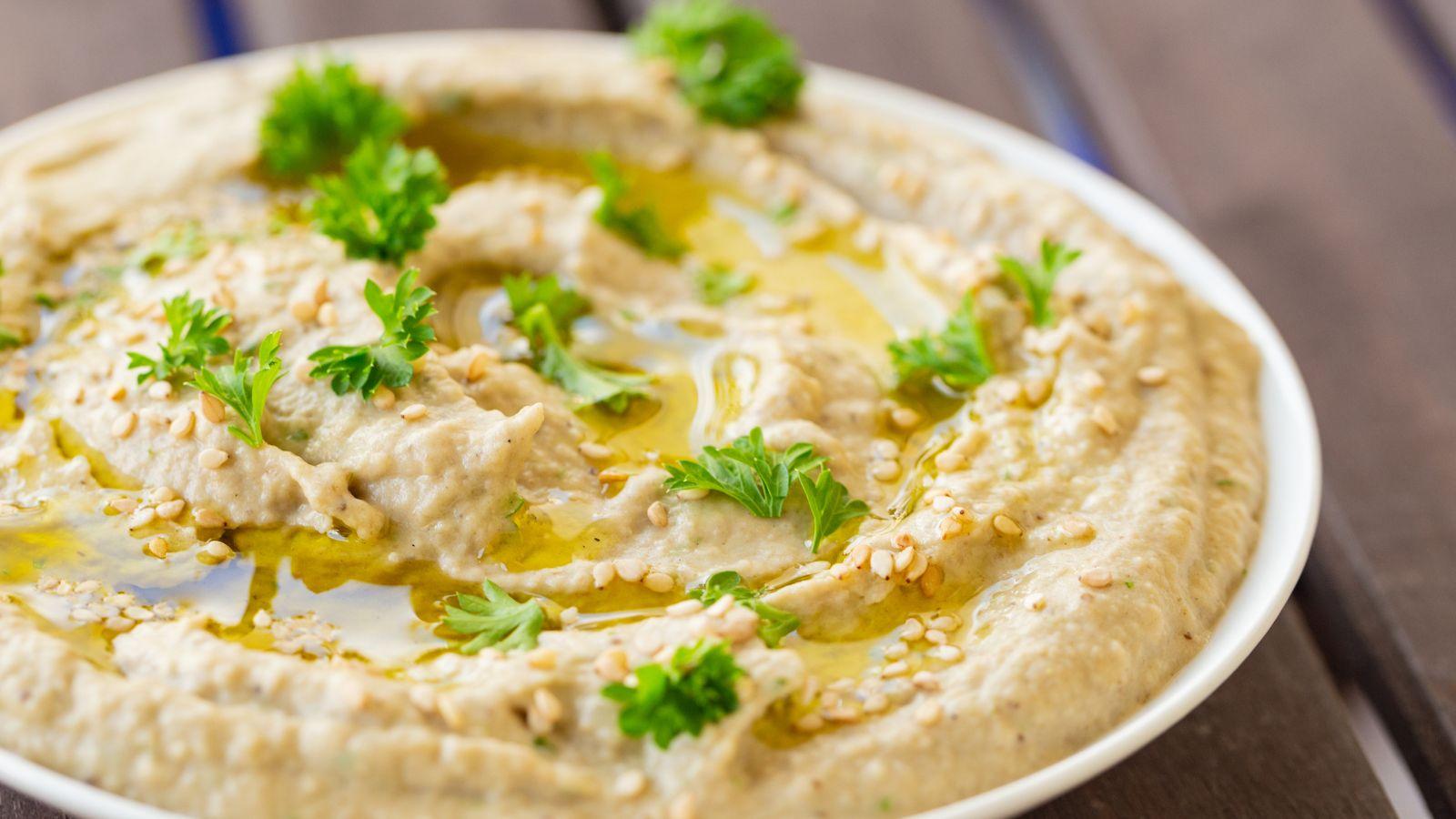 Bowl of baba ghanoush with parsley on top sitting on a table
