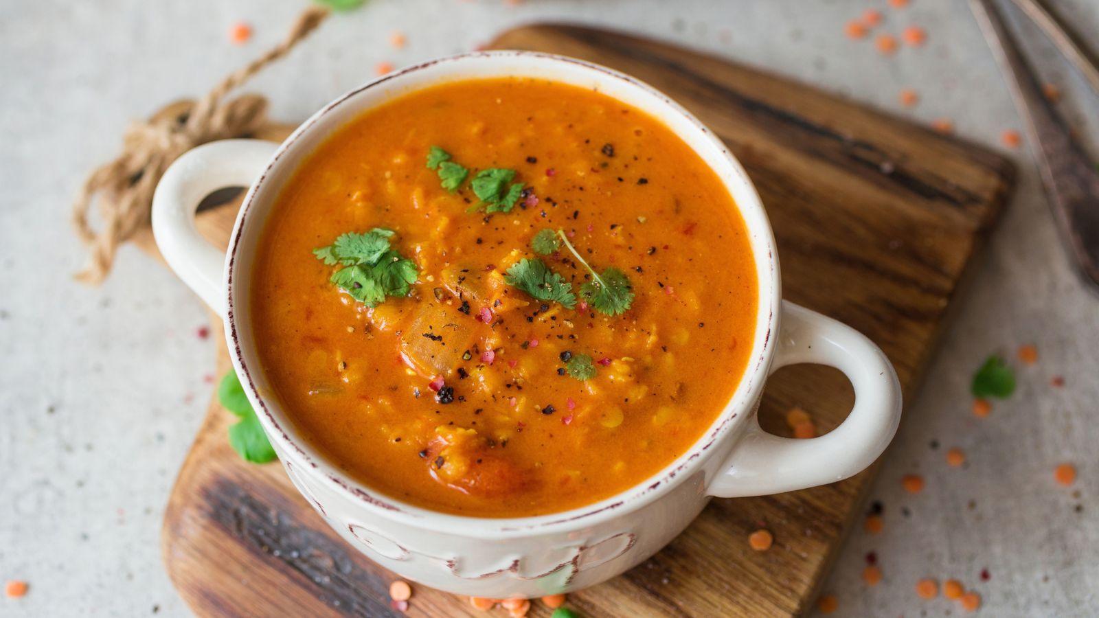 Red Lentil Soup inside a white bowl on top of a cutting board on a table
