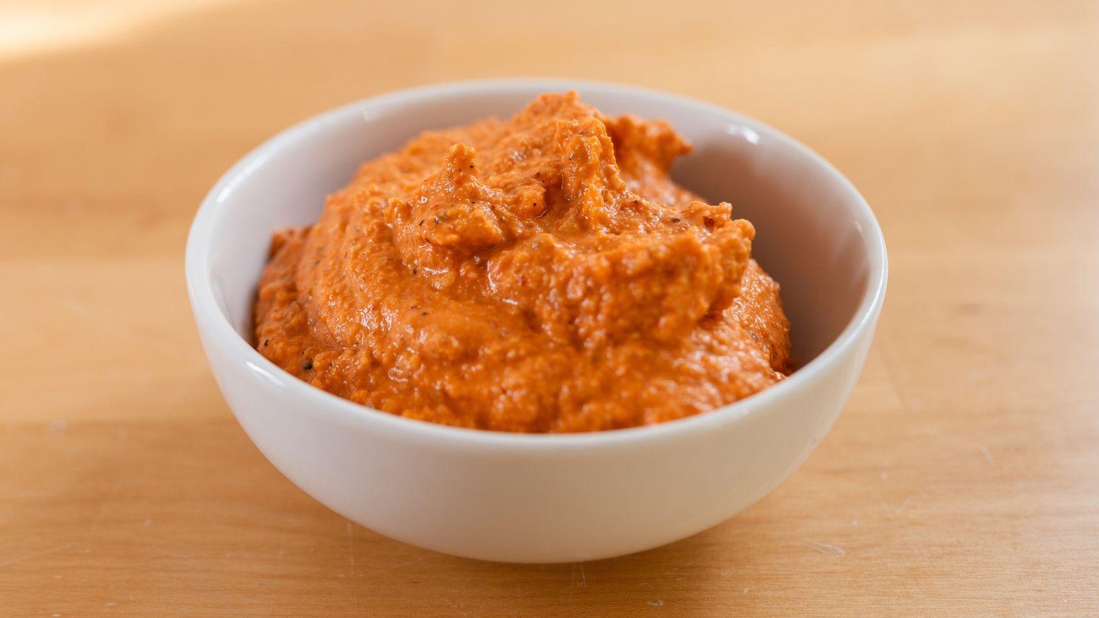White bowl of romesco sauce sitting on wood table