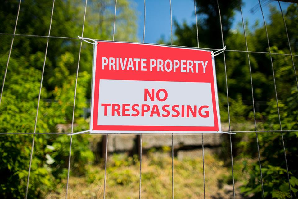 A red and white metal sign (Private Property, No Trespassing) attached to a wire fence.