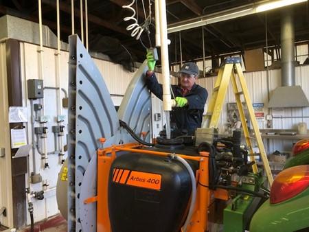 A person in work attire is filling the Arbus 400 agricultural tank with water inside a workshop.