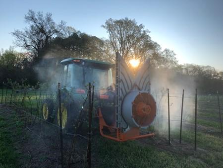 A tractor spraying water across a green field under a clear blue sky.