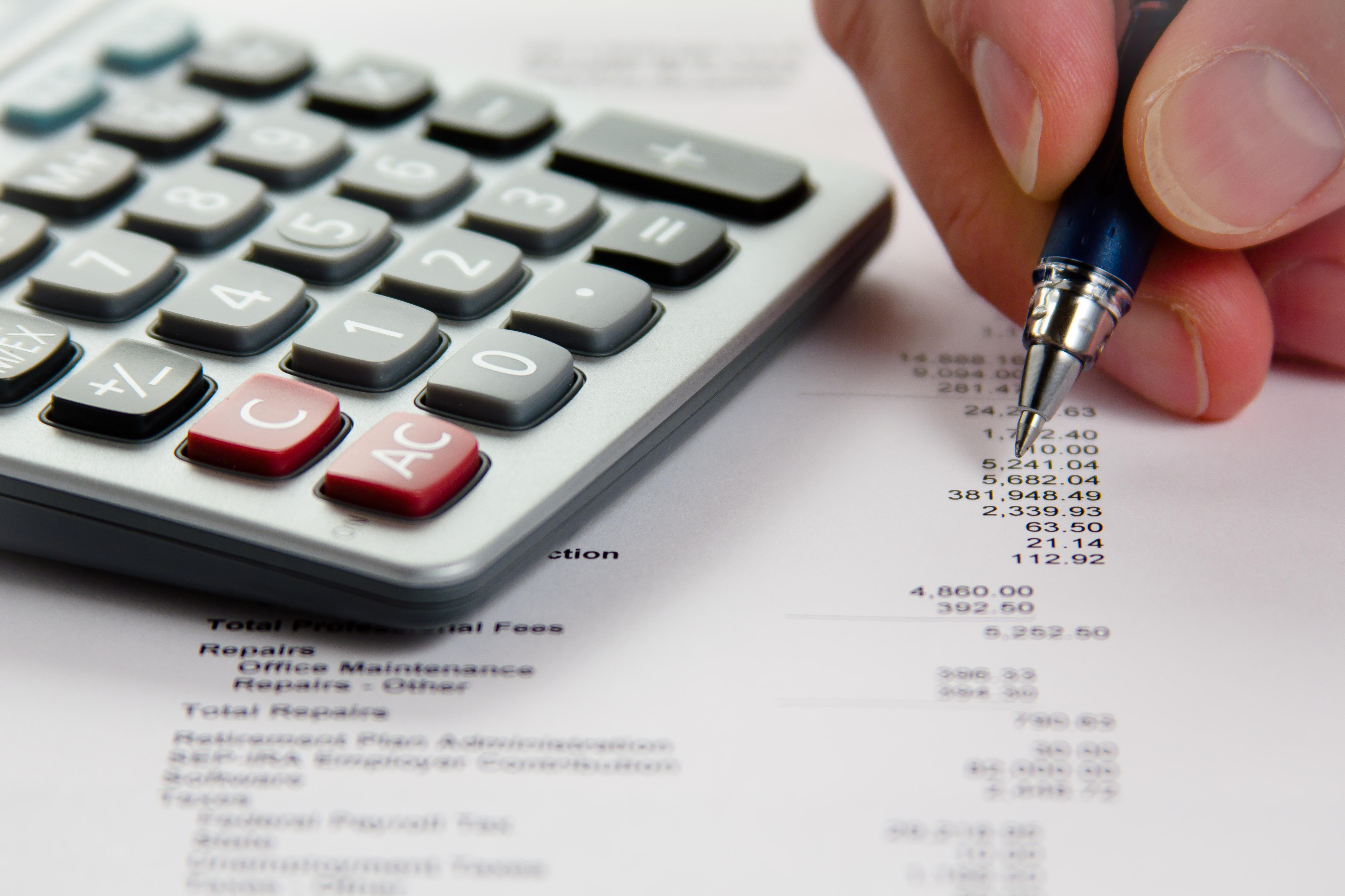 Hand holding a pen, reviewing a receipt, accompanied by a calculator