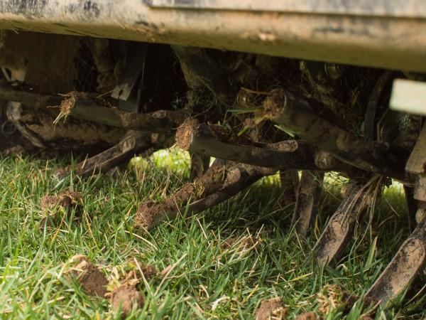 Close-up of the row of hollow tines on the underside of a lawn core aerator machine.