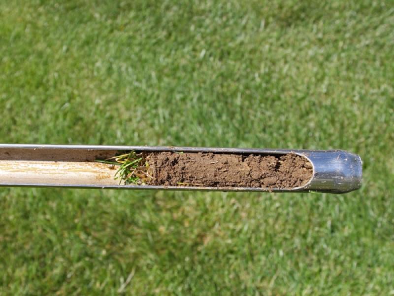 A hollow metal tube used to take soil core samples. One side has a cutout area to view the sample.