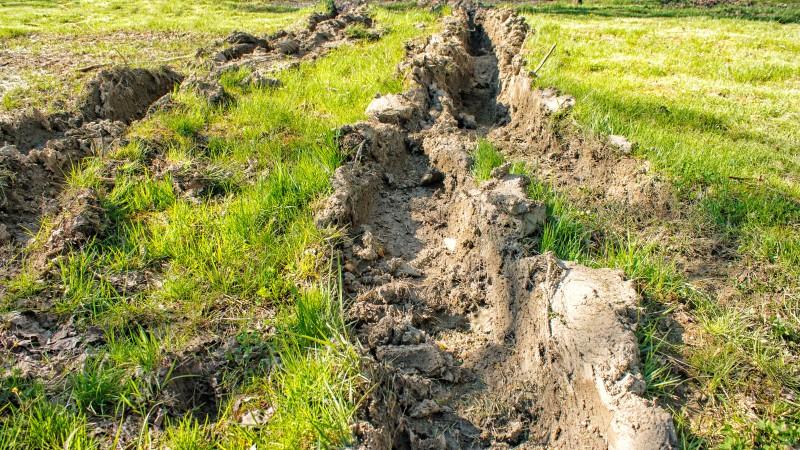 A pair of deep muddy ruts in a lawn created by vehicle tires.