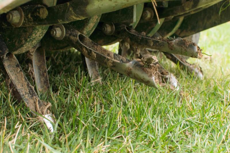 Close-up of the rows of hollow tines on the underside of a lawn core aerator machine.