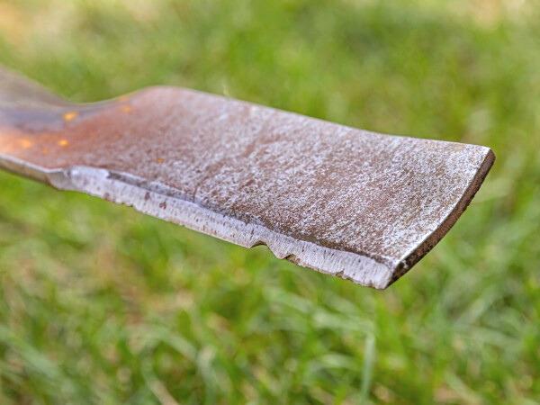 Close-up of one end of a lawn mower blade, removed from the mower. The cutting edge is dull and notched from wear.