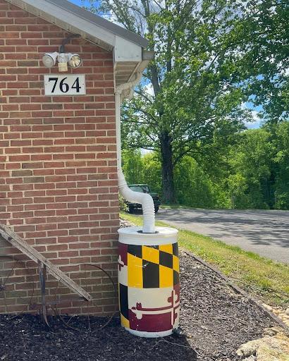 A brick building with a 55-gallon barrel attached to the downspout from the roof. The barrel is painted with the Maryland flag design.
