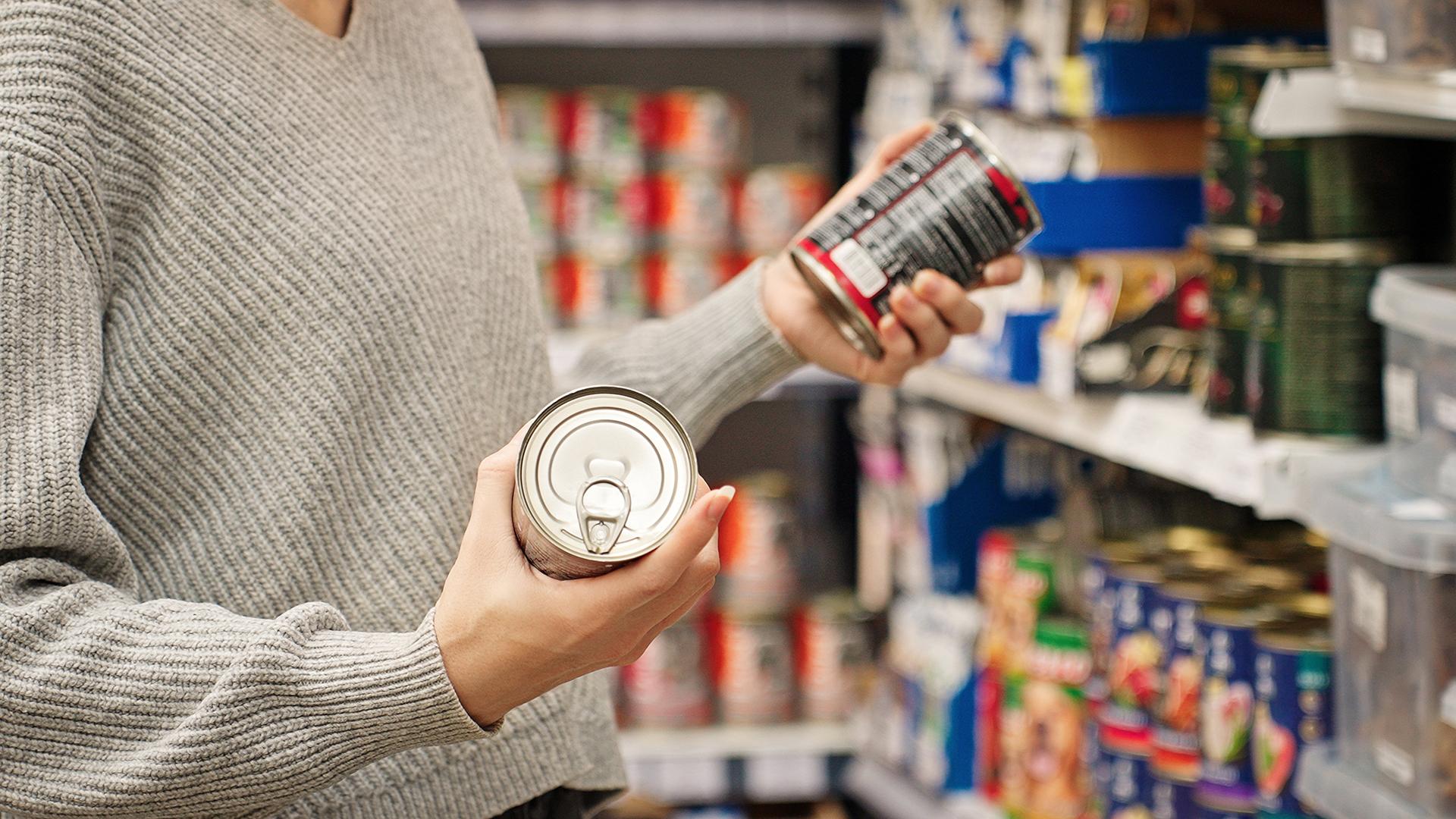 A woman looks at the nutrition labels on canned goods at a grocery store