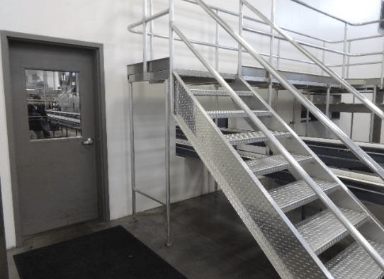 Clean industrial processing area with a metal staircase, raised platform, and door with a window; floors and surfaces appear well-maintained.