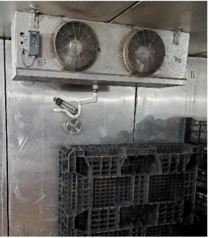 Refrigeration unit with two fans mounted above stacked plastic crates; surrounding surfaces show grime and moisture buildup.