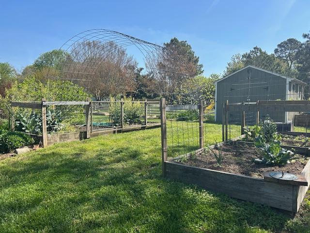 2 raised baed garden areas with a large metal fencing arch connecting them. A grass path runs underneath and between the beds with a shed in the background.