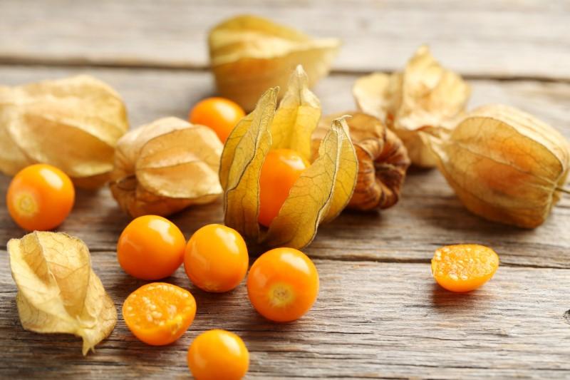 Several half-inch, orange-colored fruits removed from papery-textured, translucent, tan-colored husks on a table. A couple of fruits are visible still inside their split or intact husk.
