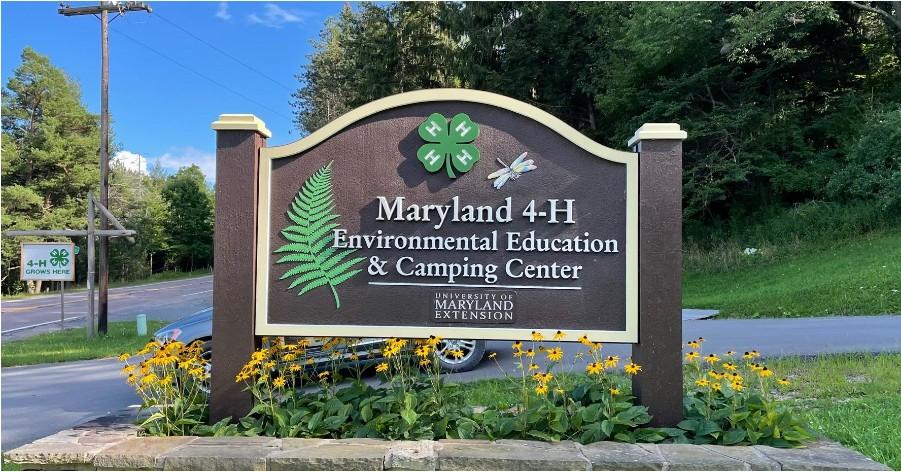 Brown sign with Maryland 4-H Environmental Education & Camping Center next to a road with 4-H Grows Here sign, with flower bed underneath