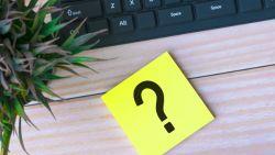 question mark on a sticky note pad sitting on a desk by a plant and a keyboard