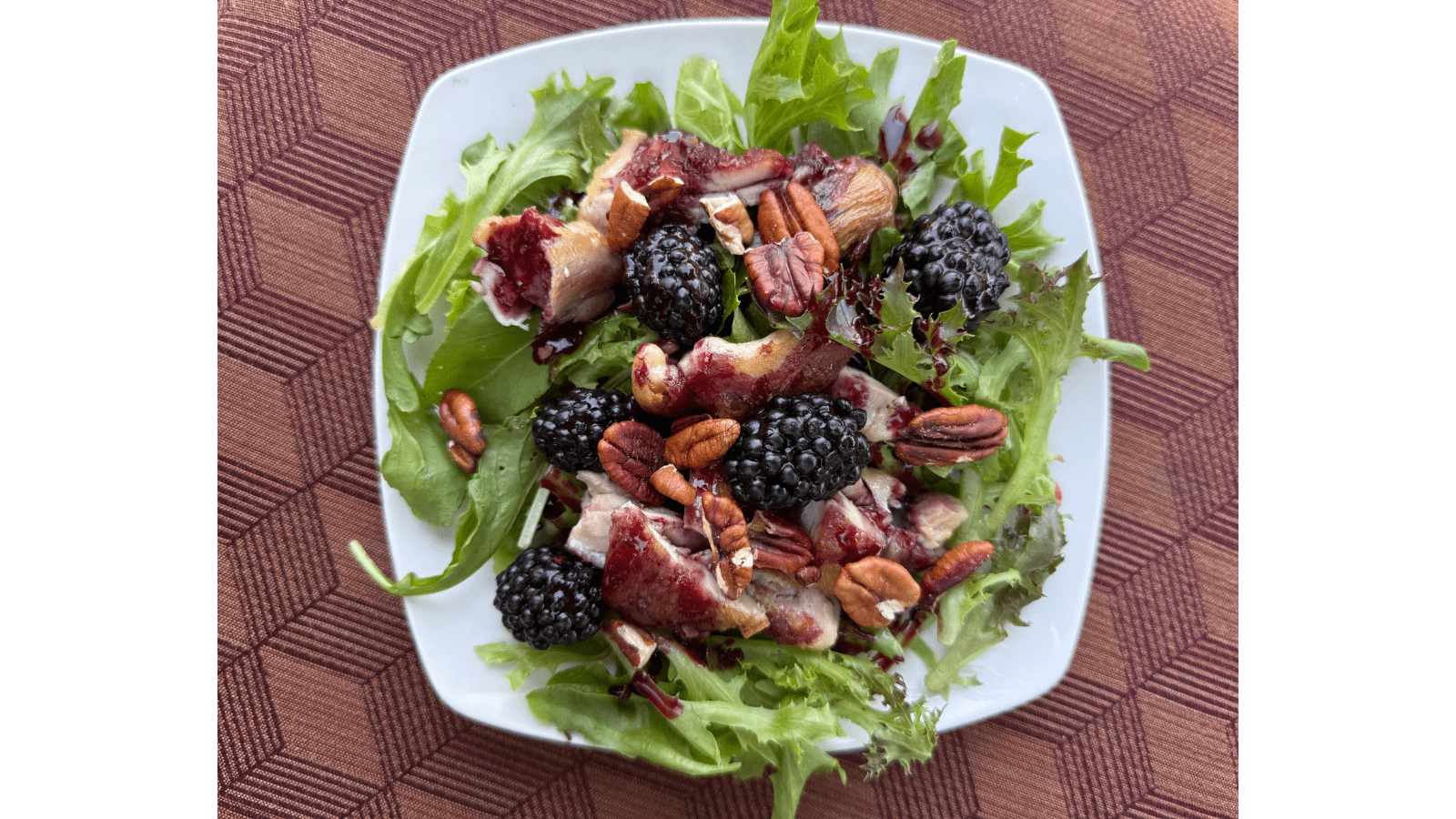 Plated salad including greens, nuts and blackberries