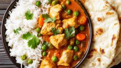 chicken curry with carrots and peas on top of rice in a bowl sitting on a table next to pita