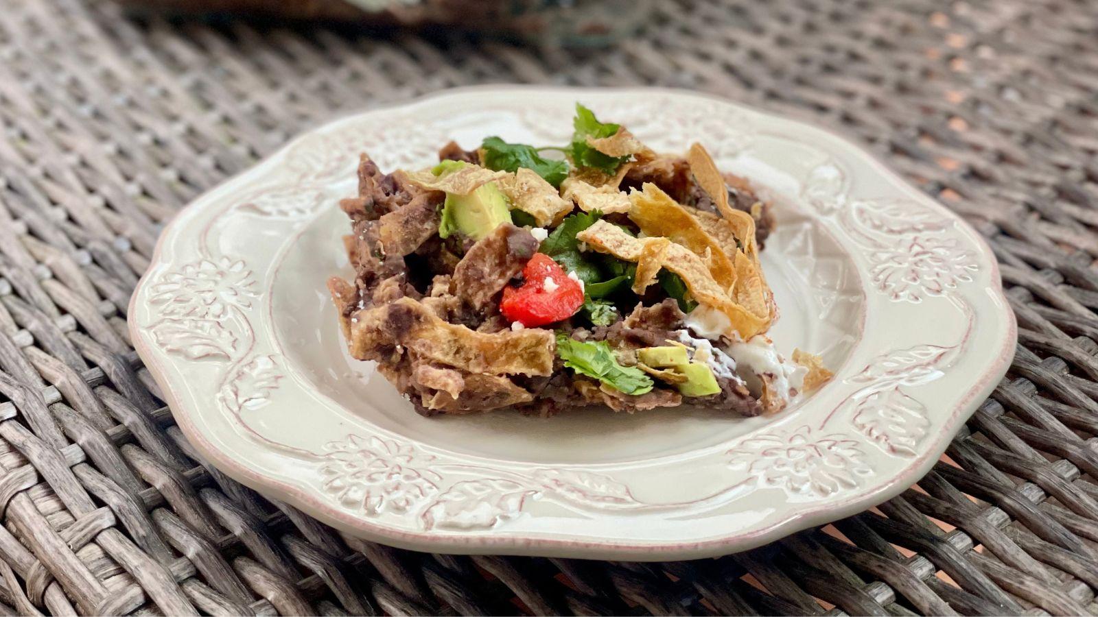 chilaquiles con frijoles on a white plate on a wicker table