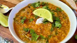 curried lentil tomato coconut soup topped with a lime wedge in a white bowl on a wooden cutting board