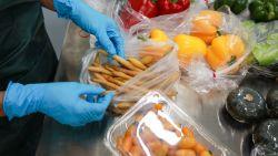  hands with blue gloves putting carrots in a plastic bag on a metal counter, assorted bagged vegetables