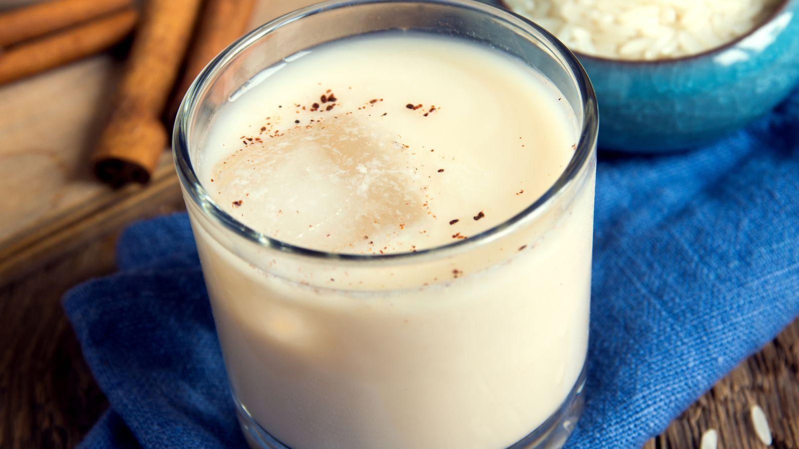 glass of horchata with ice on a blue napkin sitting on a table by cinnamon sticks