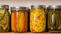 four mason jars filled with preserved food like pickles, pepper and corn