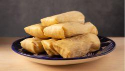 stacked tamales sitting on a dark plate on top of a wooden table with a gray background