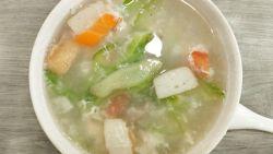 thai chicken and bitter melon soup in a white bowl on a wooden table with a spoon next to it