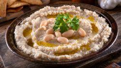bowl of white bean dip with cannellini beans and parsley on top, on a wooden table